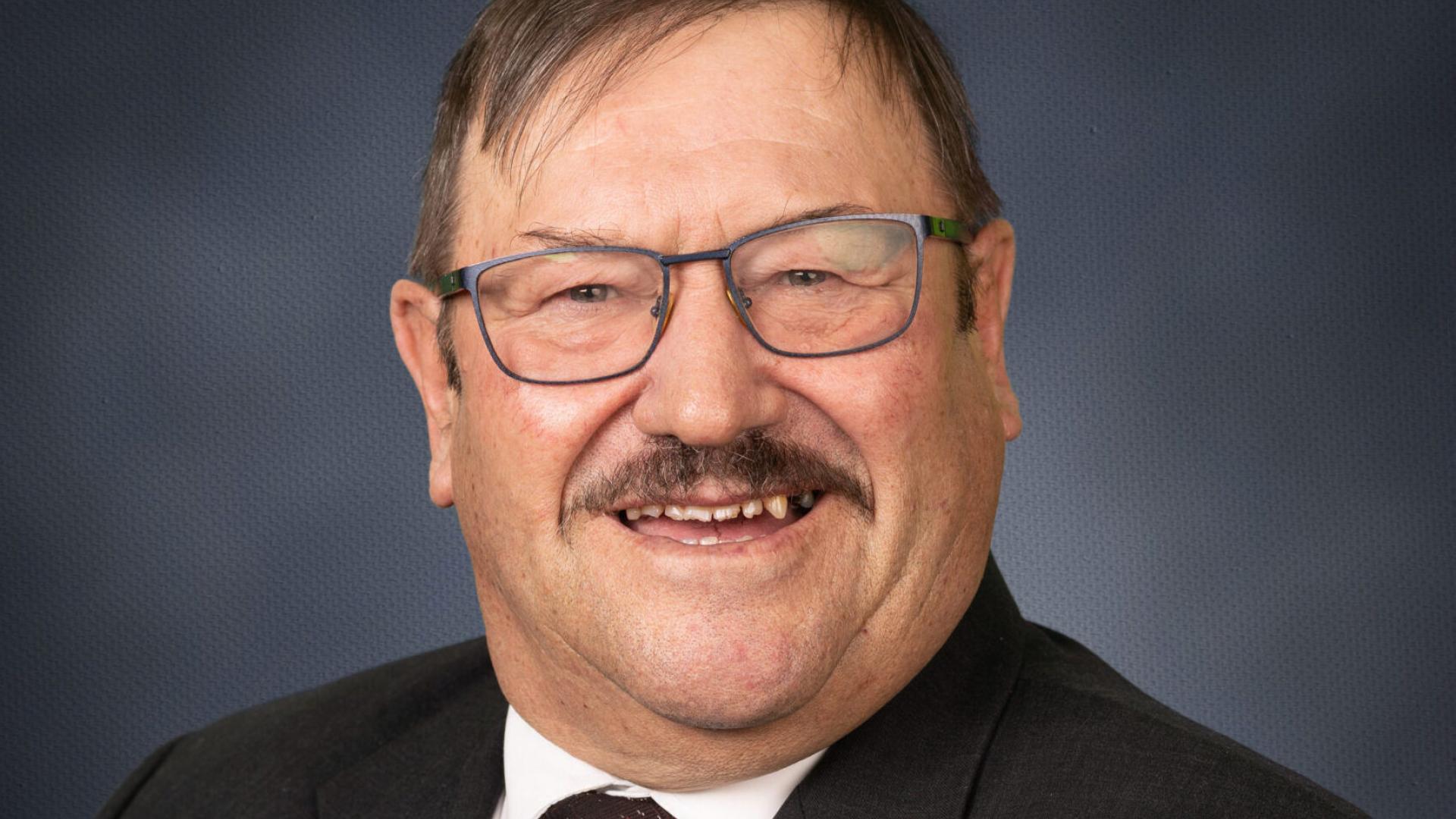 Person in a suit smiling against a dark blue background.
