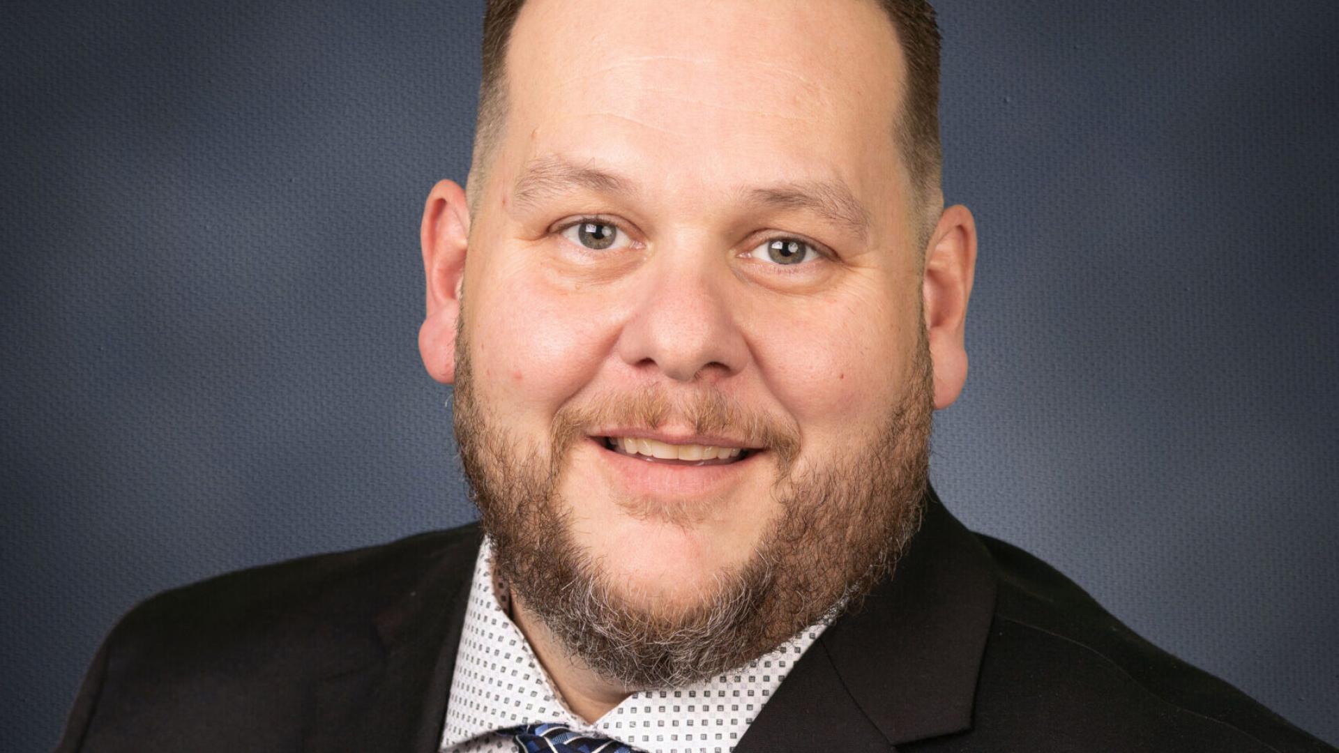 Headshot of a smiling person in a suit against a dark blue background.