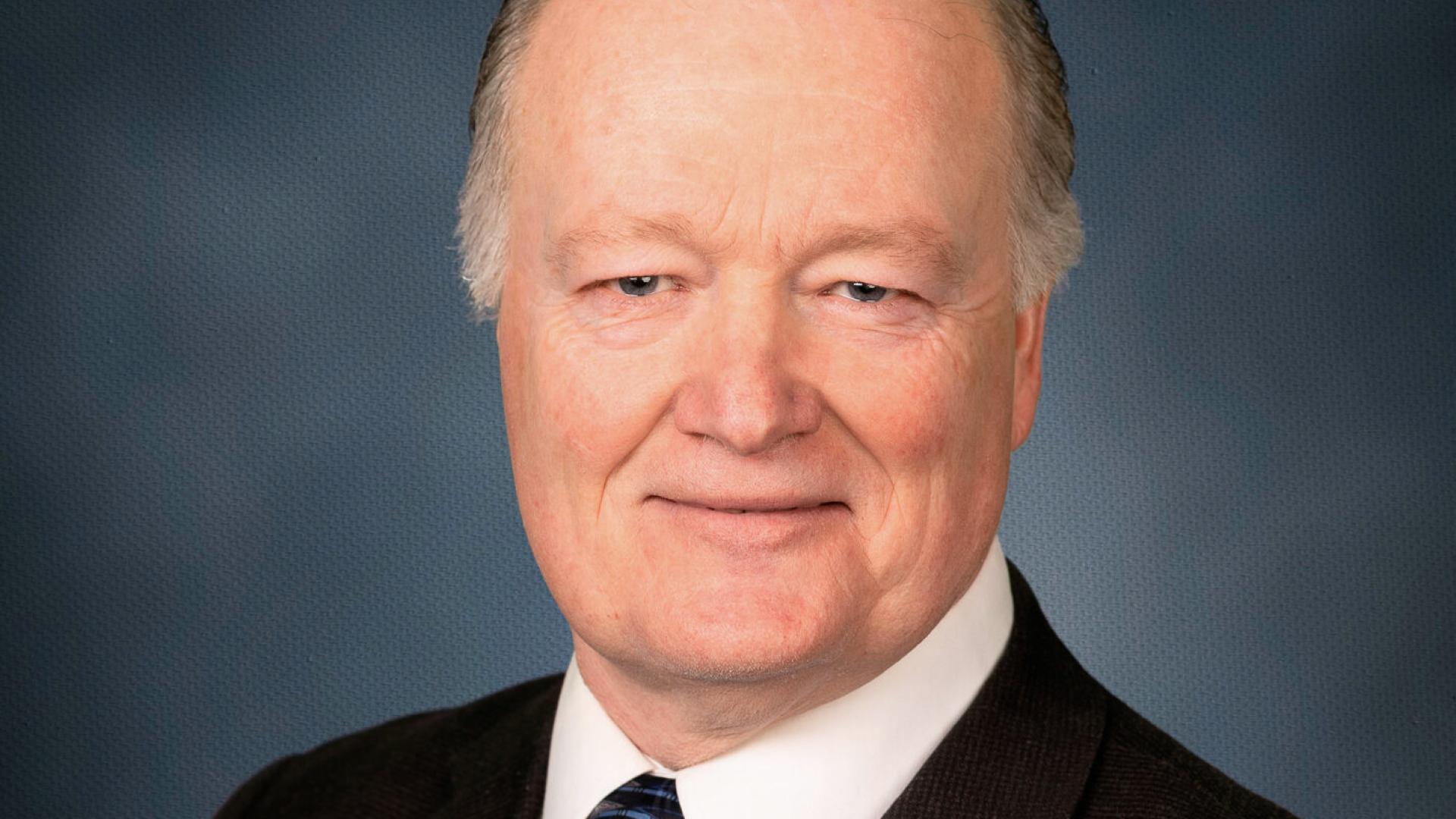 Photograph of a person in a suit with a blue background.