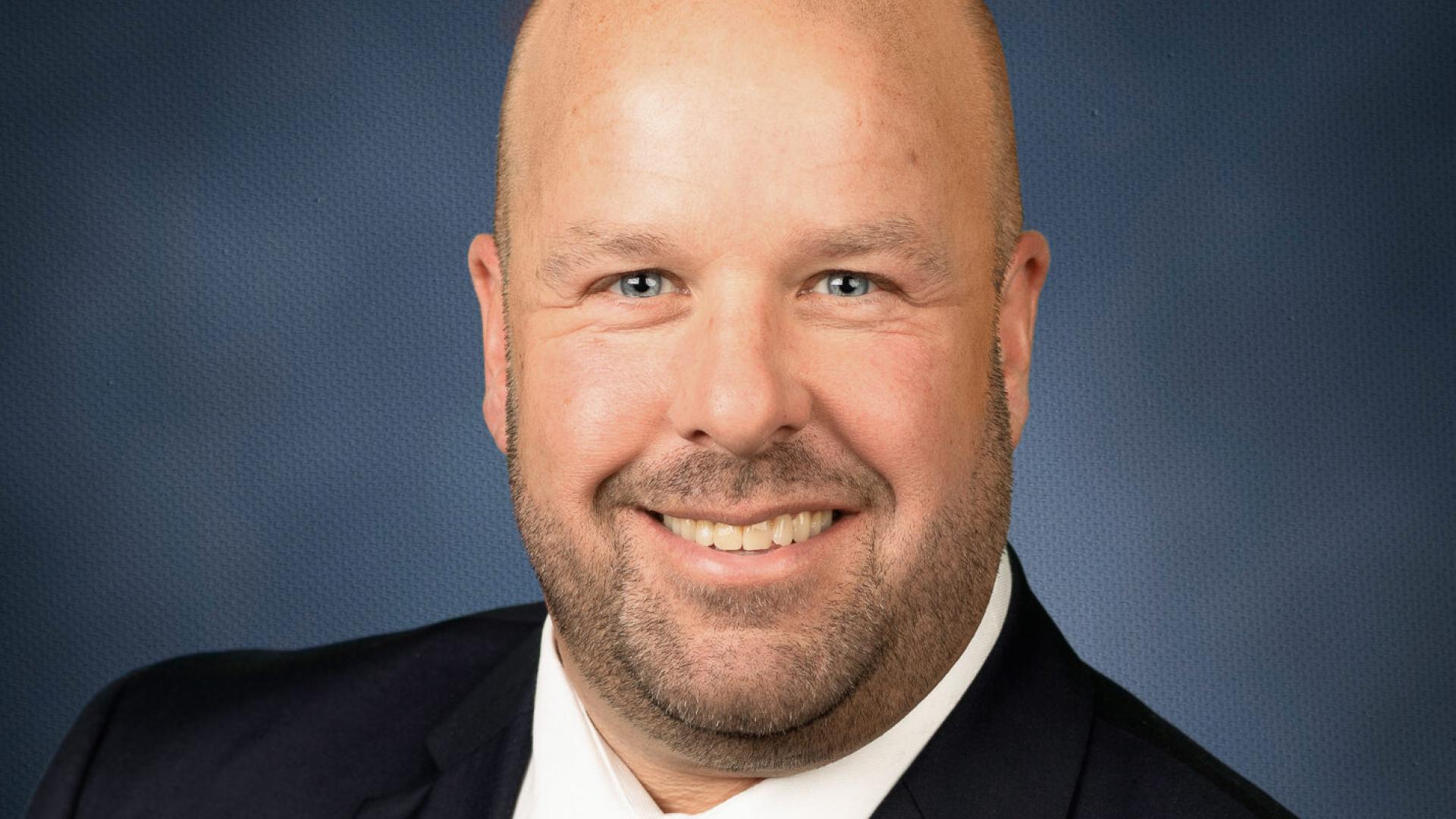 Formal portrait of a person in a suit with a striped tie, smiling.