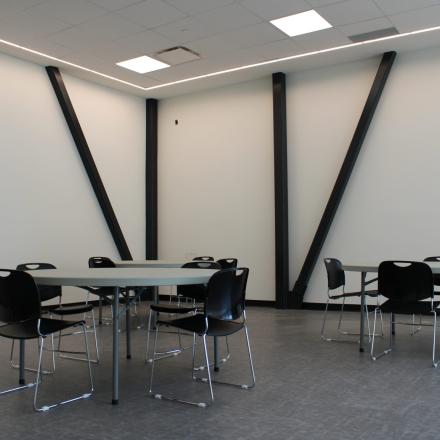 Empty room with tables and chairs, light walls, and diagonal supports.