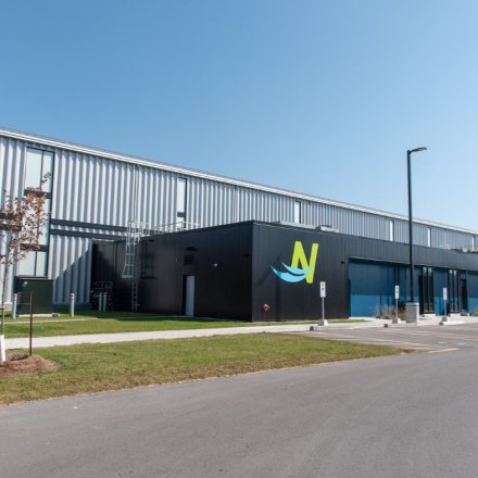 Industrial building with a logo, surrounded by grass and a clear sky.
