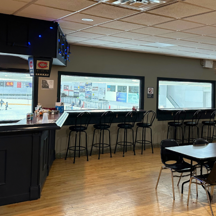 St-Isidore Arena Sports Bar featuring tables, seating, a service counter, and large windows with views of the arena.