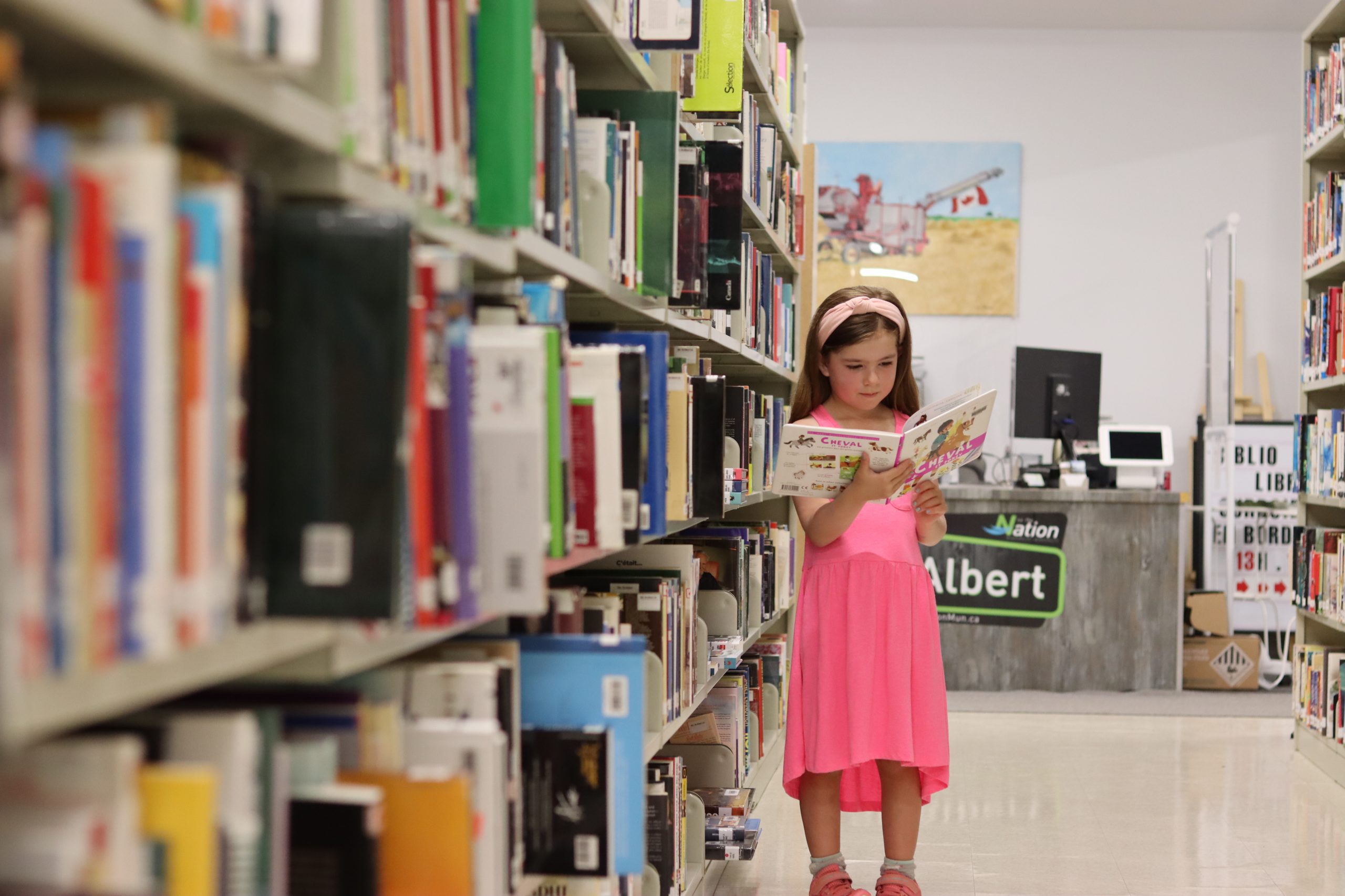 Girl in pink dress reading a book in the St-Albert Library Branch.