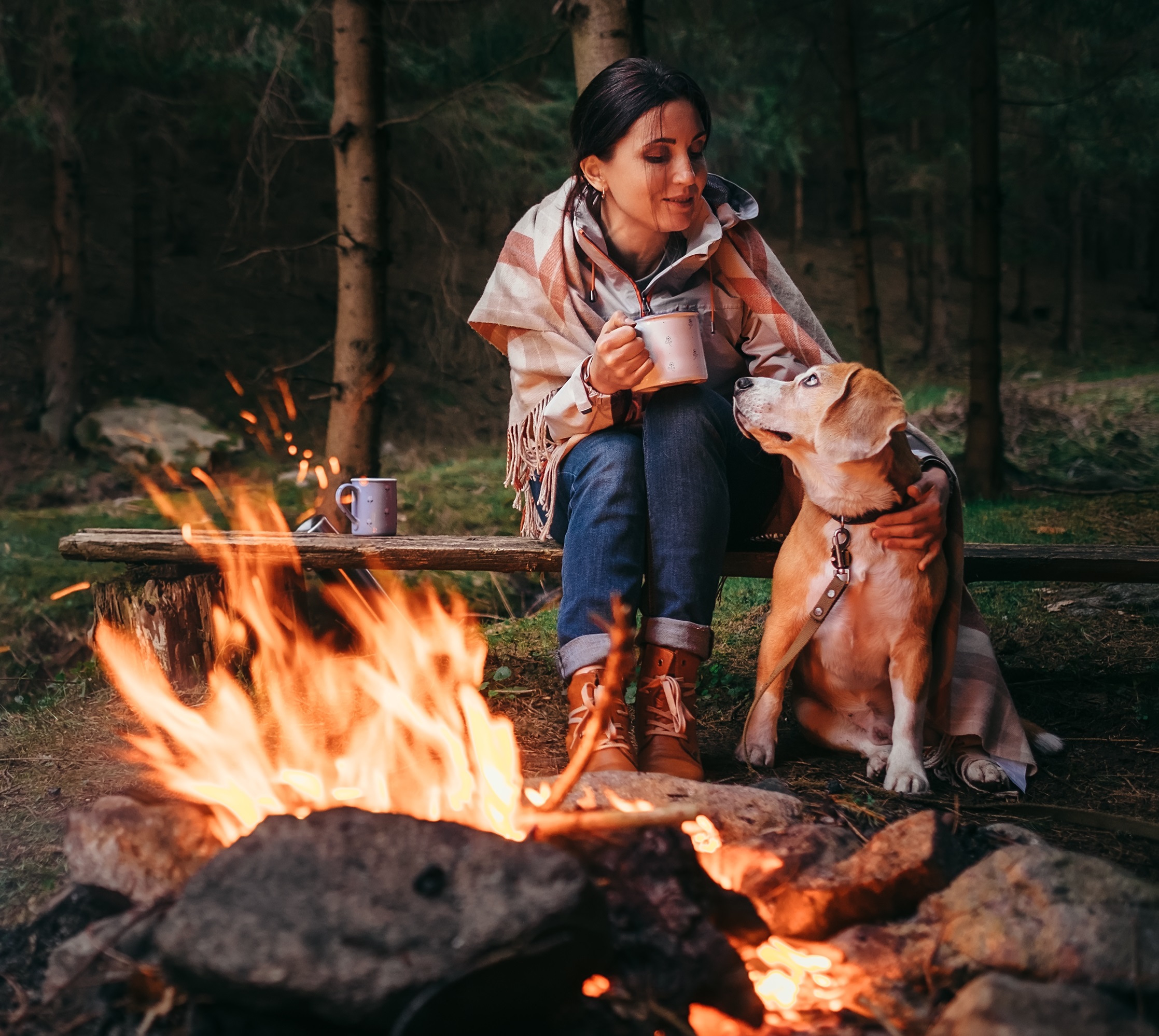Woman and her dog sitting by a camp fire. 