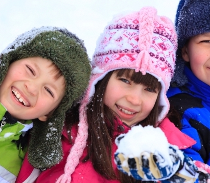 Three children holding snowballs in bright colored snowsuits and hats