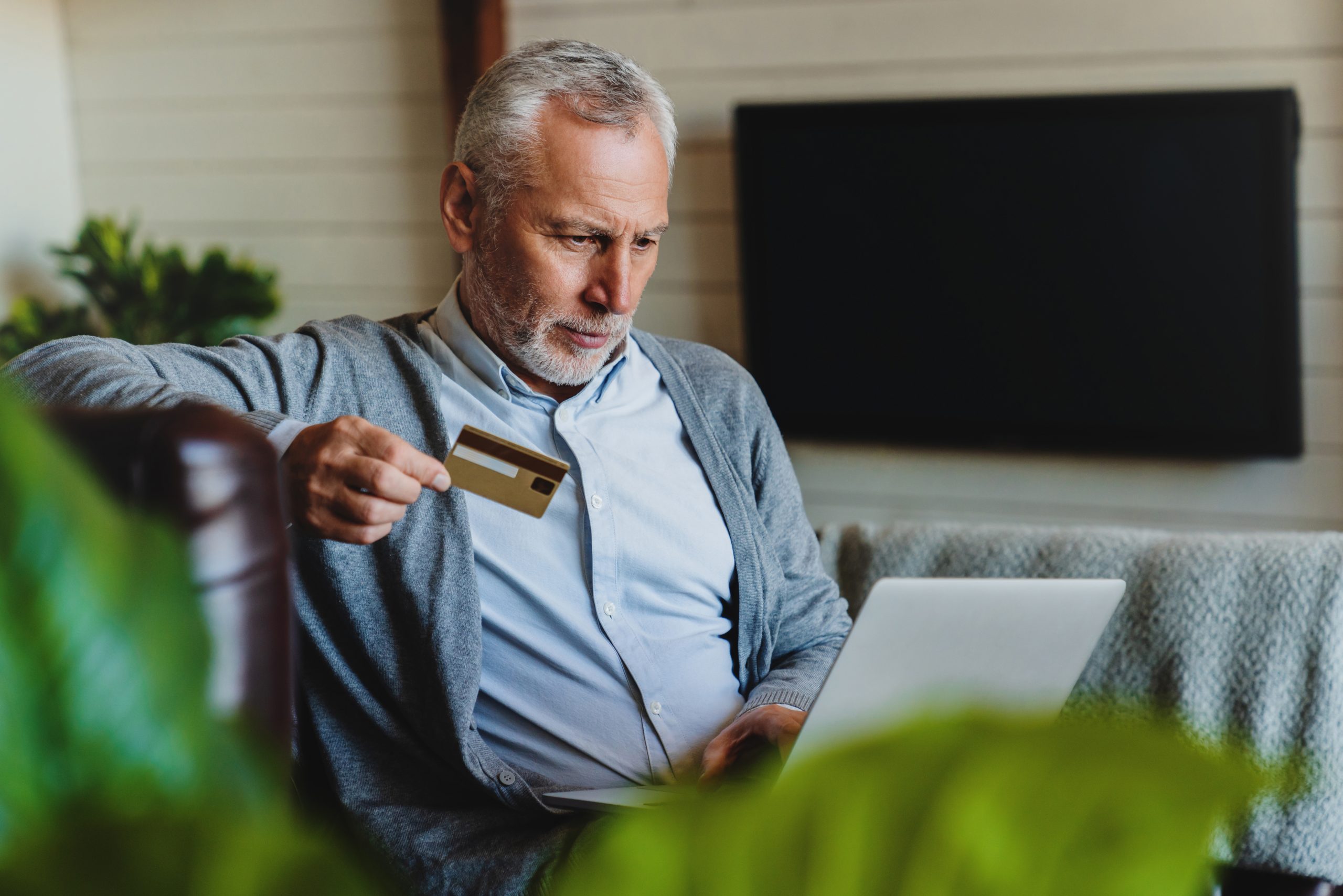 Senior man sitting on sofa with laptop and using credit card