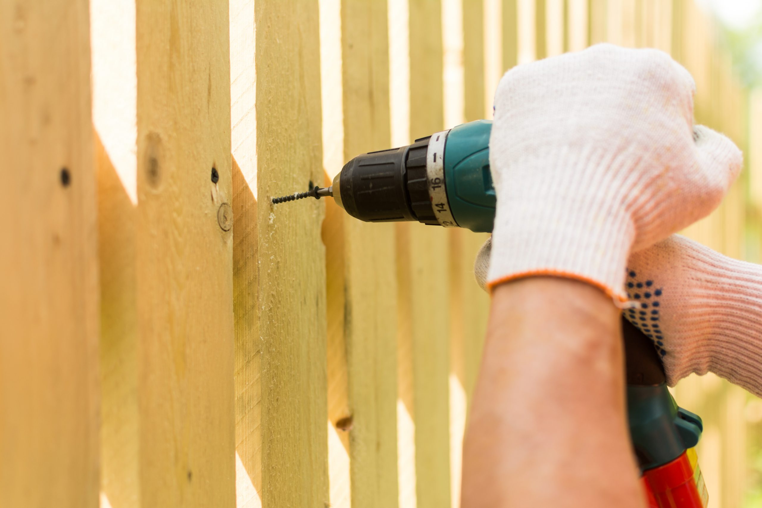Hands of the carpenter holding electric screwdriver building a fence